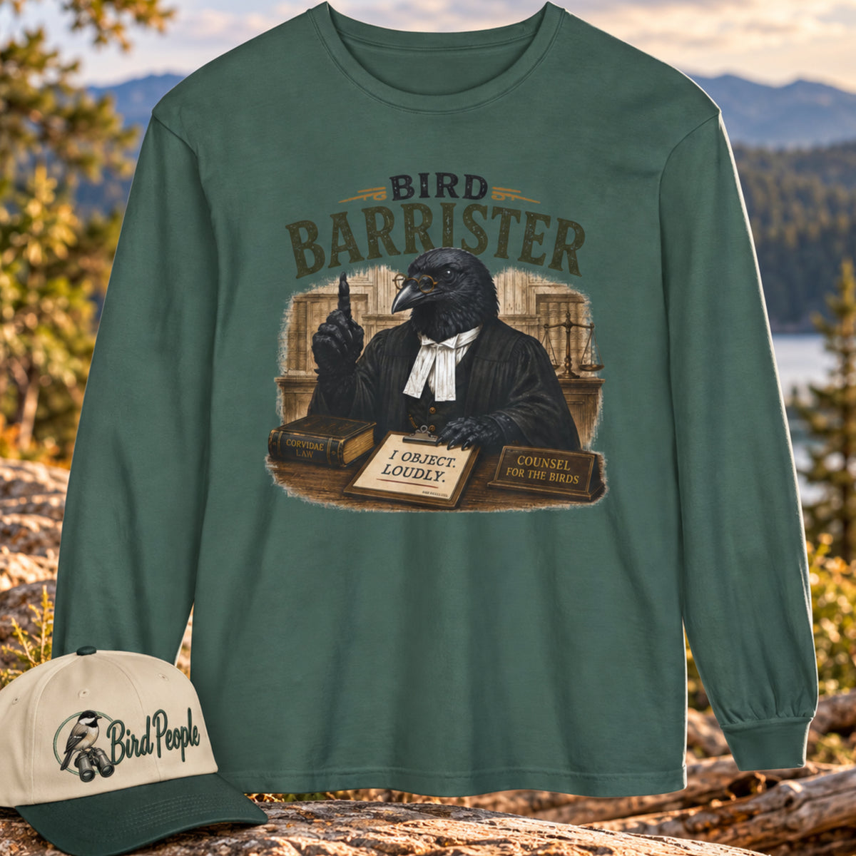 Bird Barrister crow long sleeve t-shirt in Blue Spruce teal-green, outdoors on a mountain overlook with a Bird Peeple chickadee trucker hat — funny lawyer crow design for birdwatchers.